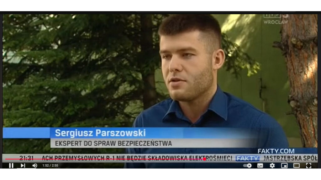 Mężczyzna w niebieskiej koszuli na tle drzew. Na dole pasek informacyjny z napisem Sergiusz Parszowski, ekspert do spraw bezpieczeństwa. Poniżej pasek informacyjny, na nim godzina i napis Fakty.com.