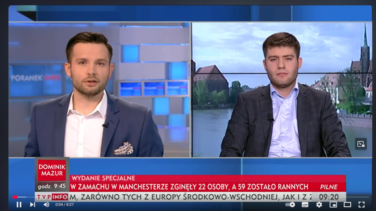 Dwóch mężczyzn w garniturach w studiu telewizyjnym podczas programu informacyjnego TVP Info Wydanie specjalne o zamachu bombowym w Manchesterze. Po lewej stronie dziennikarz, po prawej gość programu. Na dole pasek informacyjny z wiadomościami.