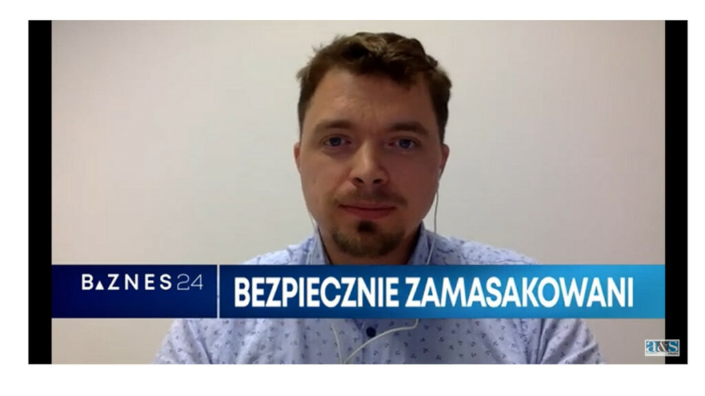 Mężczyzna w jasnej koszuli, z krótkimi włosami i zarostem. Na dole pasek z napisem: Biznes24, Bezpiecznie zamaskowani. W prawym dolnym rogu logo a&s.